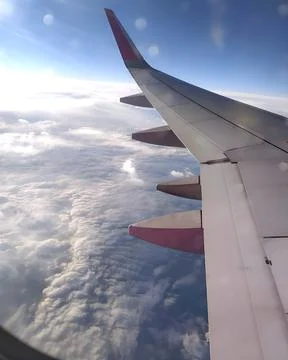 White fluffy clouds under the wing of an airplane flying over green fields .. Foto stock