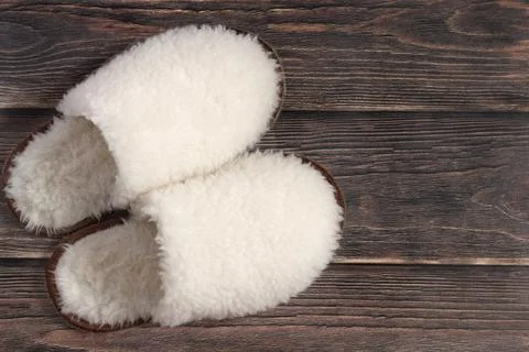 White fluffy wool slippers made of sheep's wool on a wooden background Stock Photos