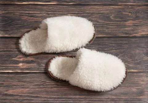 White fluffy wool slippers made of sheep's wool on a wooden background Stock Photos