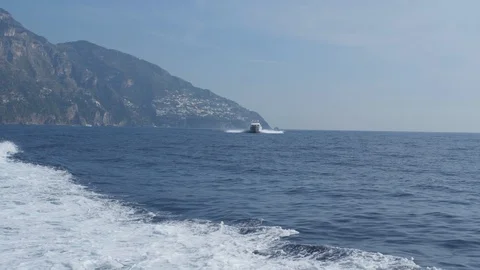 White foam track behind ship. Motor boat floats in blue sea against hilly shore Stockbeeldmateriaal 102458658