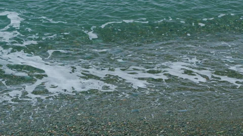 White Foam Wave Beaching On Sea Shore Pebbles. Pebble Beach Foam Sea Surf. Still Stock Footage 257651274