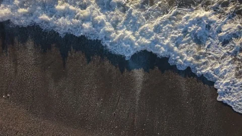 White foaming waves rolling ashore on sandy beach .Very low and close drone Stock Footage 341111338