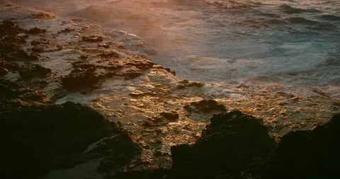 White foamy ocean waves breaking on rocky beach at golden sunset light. Close-up Stock Footage 238682329