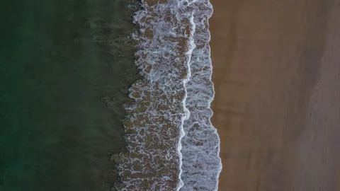 White foamy waves breaking between the dark sand and the deep ocean water Foto stock