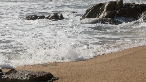 White foamy waves lap on the sandy beach with sandstone rocks in background Stock Footage 103641873