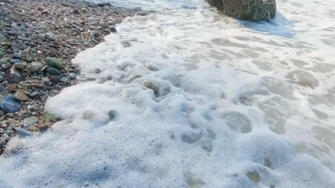 White foamy waves splashing on various shape and color pebbles beach or seashore Stock Footage 235583548