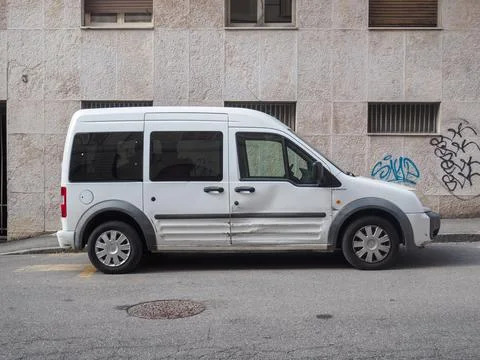 White Ford Transit Connect van parked by graffiti covered building, side pane Fotos Stock