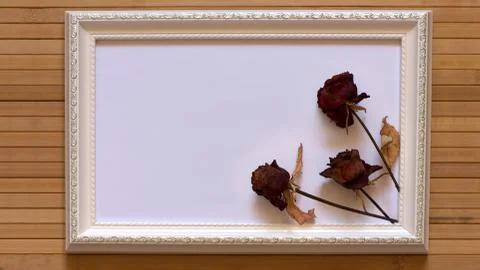 White frame with three dried red roses and empty place for text on bamboo wall. Foto stock