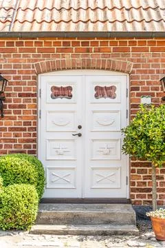 White front door with small square decorative windows and flower pots with red Stock Photos
