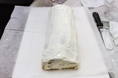 White frosted rectangular cake on parchment paper during dessert preparation. Stockfoto's