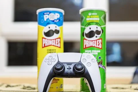 White game controller with Pringles potato chips cans in the background. Stock Photos