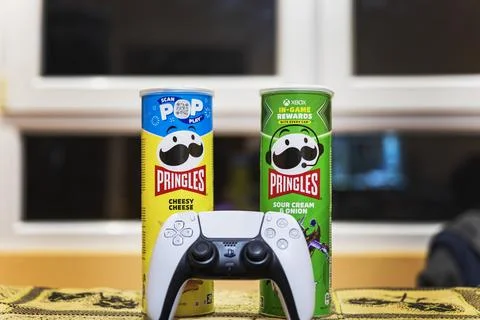 White gaming console controller on a table with potato chips cans. Stock-Fotos