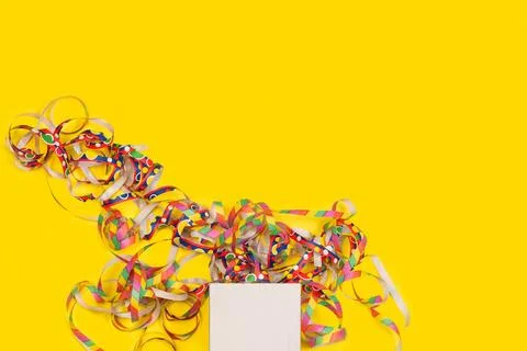 A white gift box and colored paper serpentines on a yellow background Stock Photos
