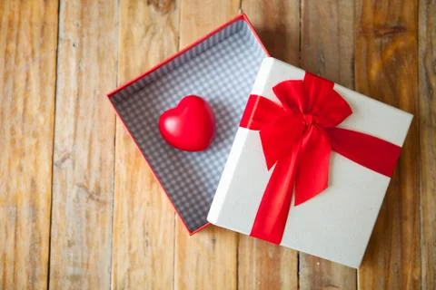 White gift box and red ribbon and mini heart inside on wood background with s Foto stock