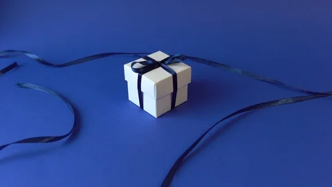 White Gift box with classic blue ribbon on blue surface. Top view Stock Footage 121843437