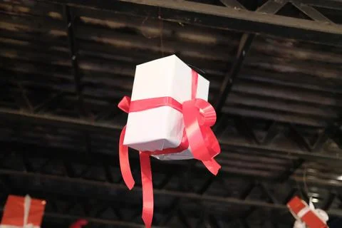 White gift box decorated with red ribbon hanging from ceiling beams Stock Photos
