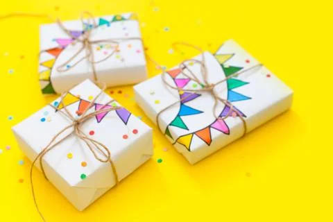 White gift box. Drawing of a colored garland, flags. Yellow background. Confetti Stock Photos