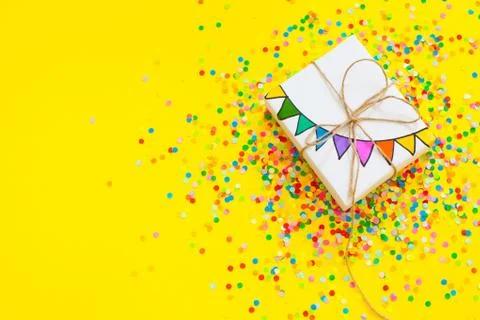 White gift box. Drawing of a colored garland, flags. Yellow background. Confetti Stock Photos
