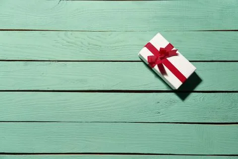 White gift box with red bow on green wooden planks Stock Photos