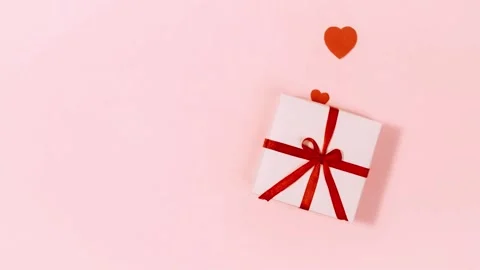 White gift box with red ribbon and flying hearts on soft pink background. Stock Footage 345112923