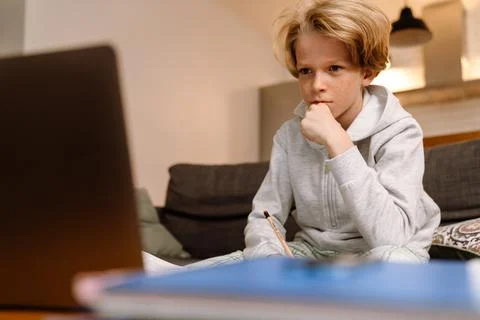 White ginger boy writing in exercise book and using laptop Stock Photos
