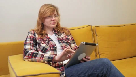 White girl communicates on the tablet while sitting on the couch Stock Footage 233489727