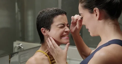 White Girlfriends Plucking Eyebrows Together in Bathroom at Home Stock Footage 100568973