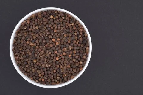 White glass bowl of black pepper. Isolated on a dark grey background. Top vie Stock Photos