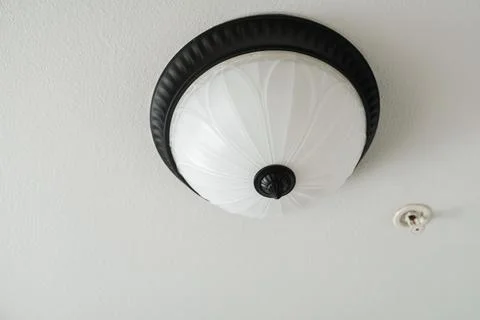 A white glass dome ceiling light fixture with a dark bronze metal rim on a te Stock Photos