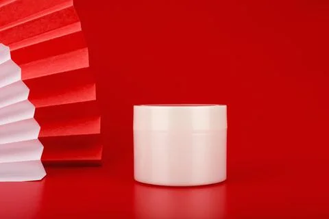 White glossy cream jar on red background with red waver from the left side Stock Photos