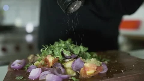 A white-gloved chef sprinkles pepper from a hand mill on chopped vegetables on a Stock Footage 243344500