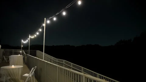 White glowing string lights hanging outdoors at night, creating a cozy Stock Footage 317329223