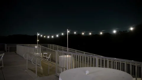 White glowing string lights hanging outdoors at night, creating a cozy Stock Footage 317733344