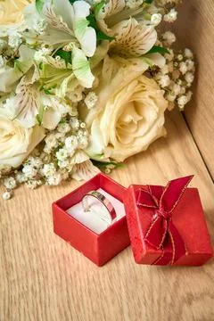 White gold ring in a red gift box, bouquet of white flowers on a wooden bac.. Stock Photos