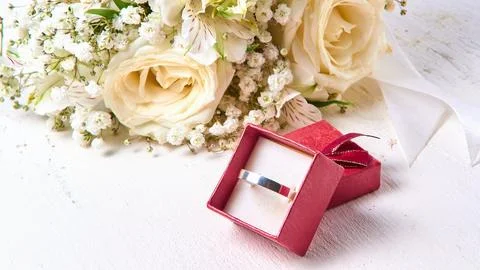 White gold ring in red gift box and bouquet of flowers on white textured wood Stock Photos