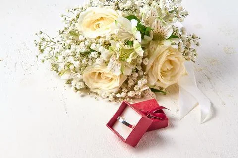 White gold ring in red gift box and bouquet of flowers on white textured wo.. Stock Photos