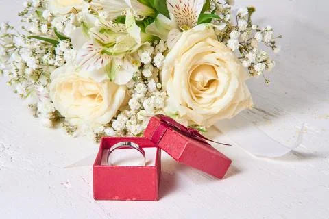 White gold ring in red gift box and bouquet of flowers on white textured wood Stock Photos