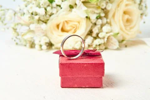 A white gold ring stands on a red gift box and a bouquet of flowers on a wh.. Stock Photos