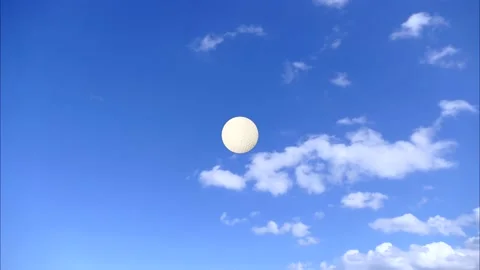 A white golf ball falls from the sky down to the earth - blue sky &amp; white clouds Stock Footage 137868938
