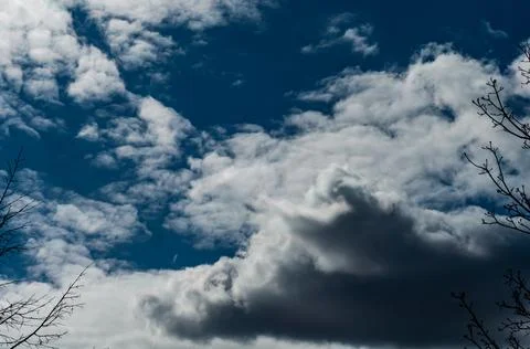 White-gray cloudy clouds against dark blue sky, the sun came out from behind  Stock Photos