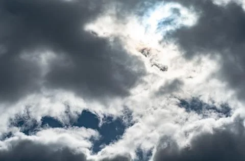 White-gray cloudy clouds against dark blue sky, sun came out from behind clou Stock Photos