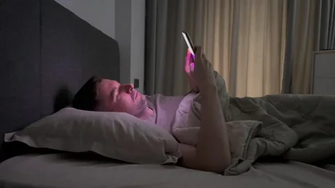 White guy lying in bed scrolling through social media feed, then puts phone away Stock Footage 283400646
