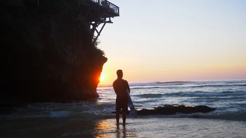 White guy stands in a bay on the ocean with a surfboard and looks into distance Stock Footage 105007333