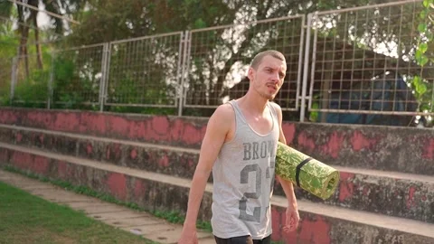 A white guy walks around the stadium with a sports mat in his hand. Video stock 231336864