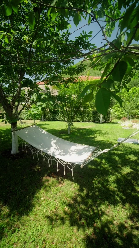 White hammock between trees in a sunlit Mediterranean garden Stock Footage 327013612