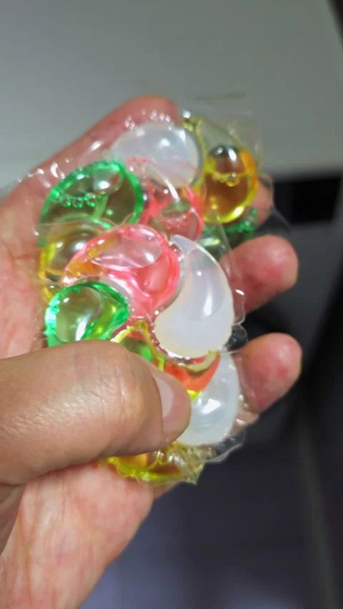 White hand holding washing machine detergent capsules Stock Footage 273872943