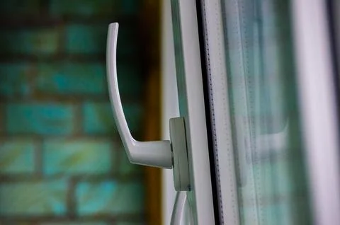 A white handle on a window is shown against a green brick wall. Foto stock