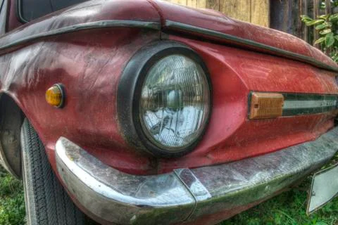 White headlight in a black frame of a red car with a silver bumper Stock Photos