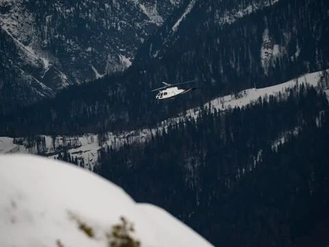 White helicopter flies over snowy forest on a cloudy day Stock Photos