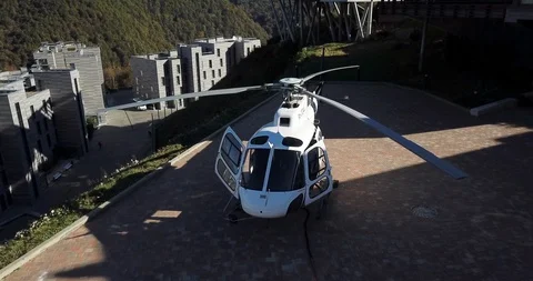 White helicopter standing on takeoff site in luxury mountain city aerial view Stock Footage